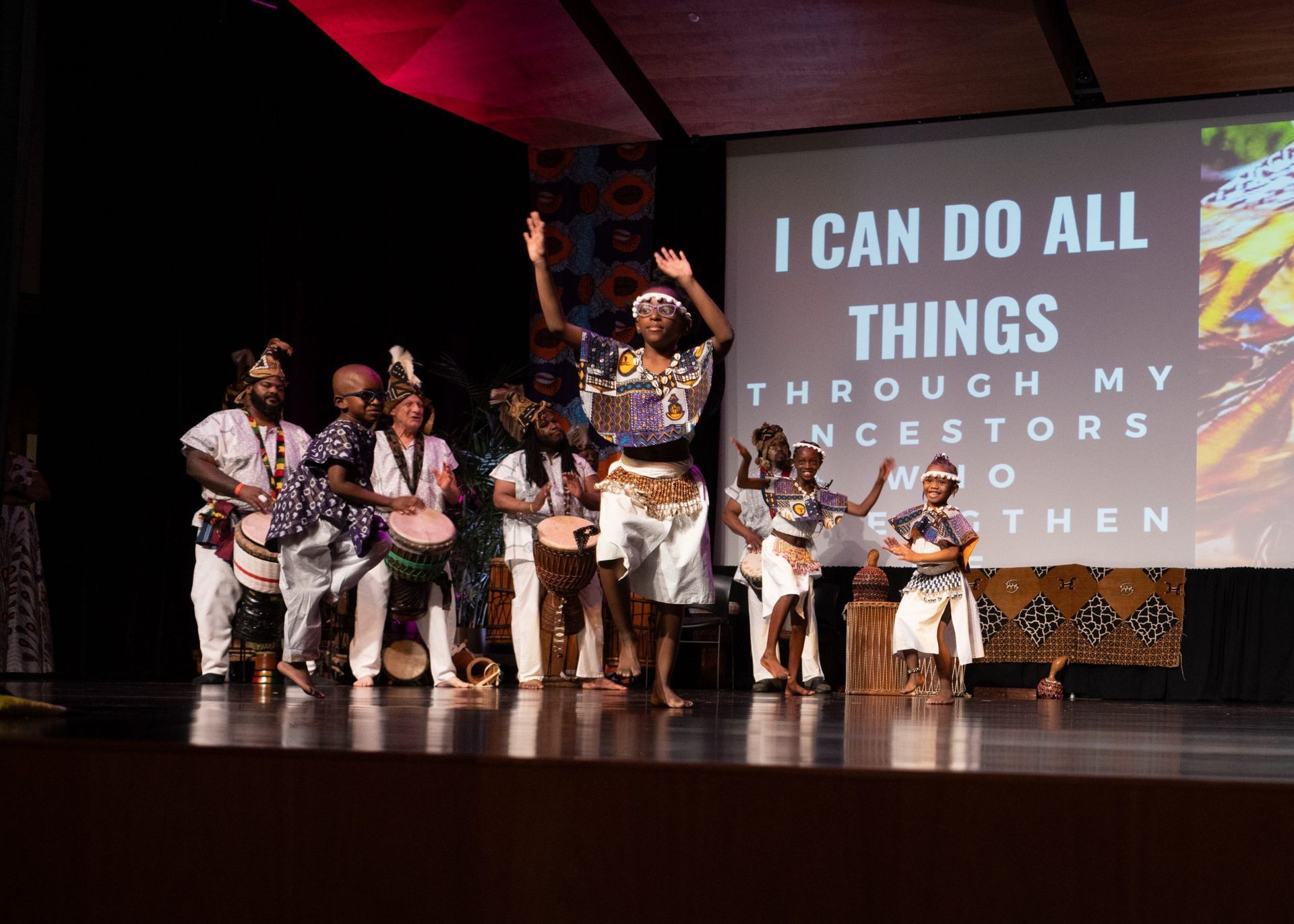 People in African attire performing on stage, drums and text 