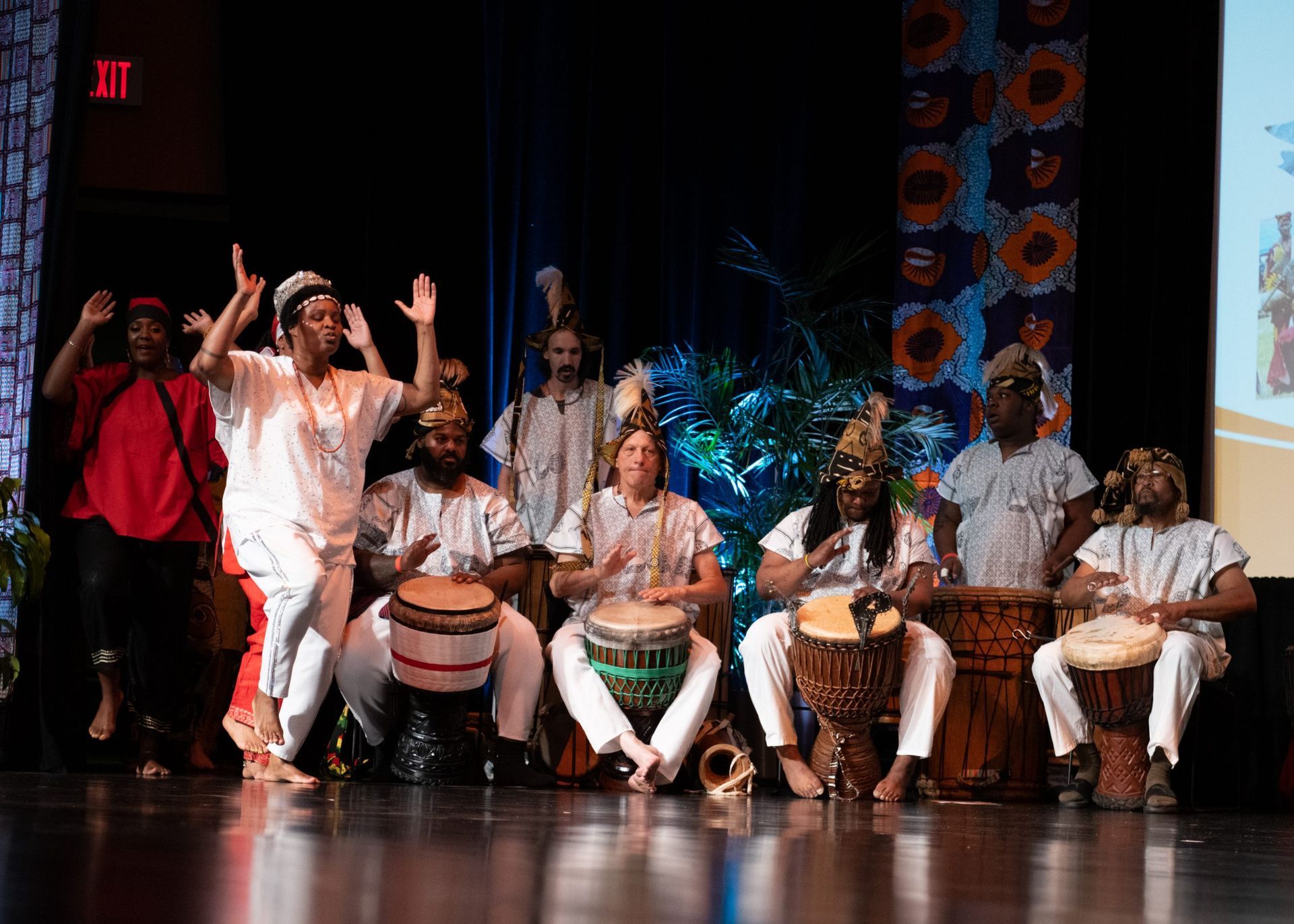 A group of musicians on stage, playing drums and dancing, with a colorful backdrop.