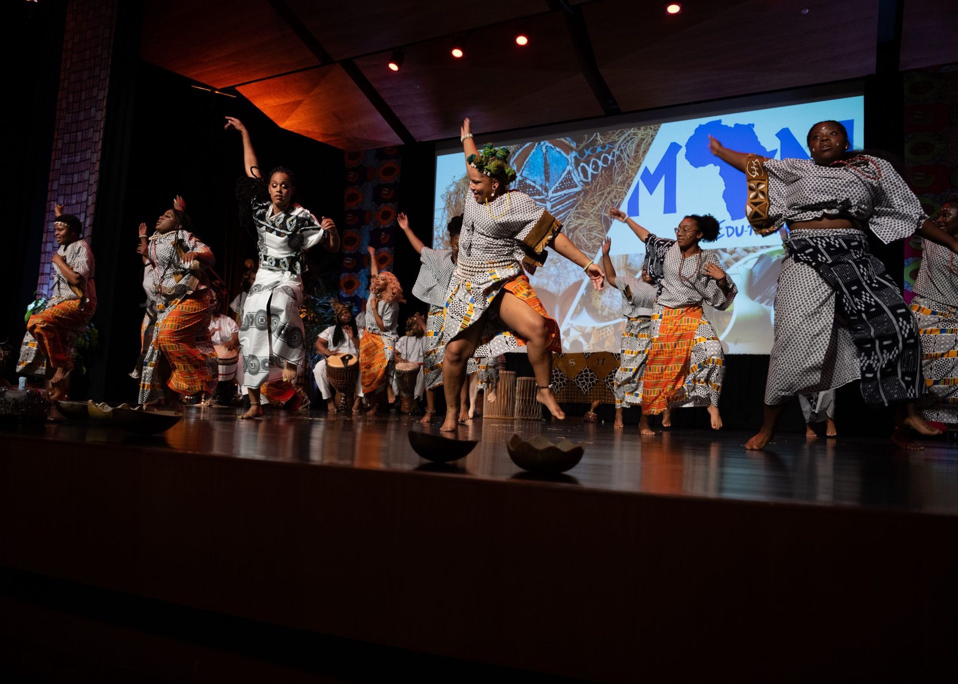 African dancers on stage in colorful outfits, performing with energy.