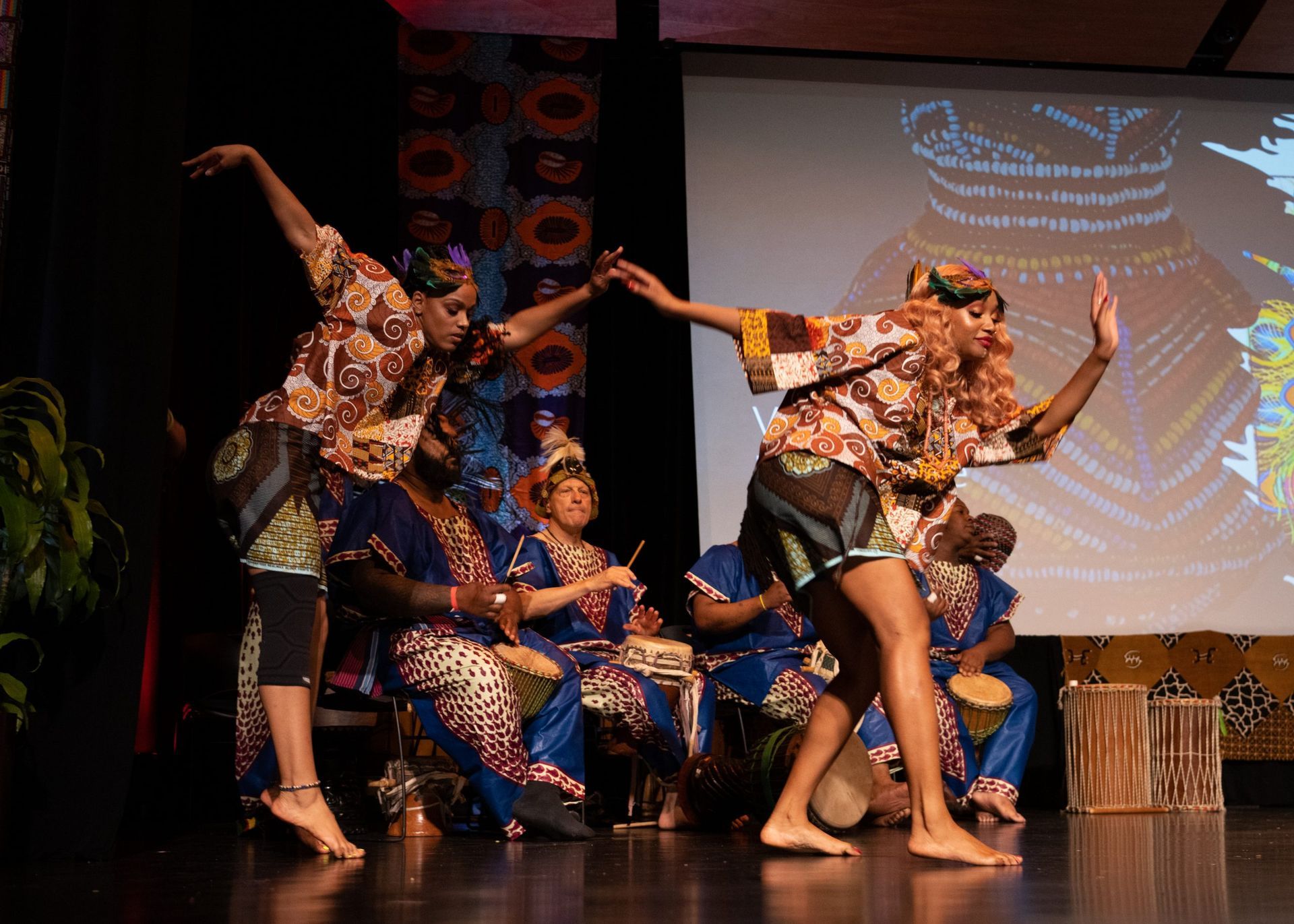 African dancers in colorful attire perform on stage with drummers.