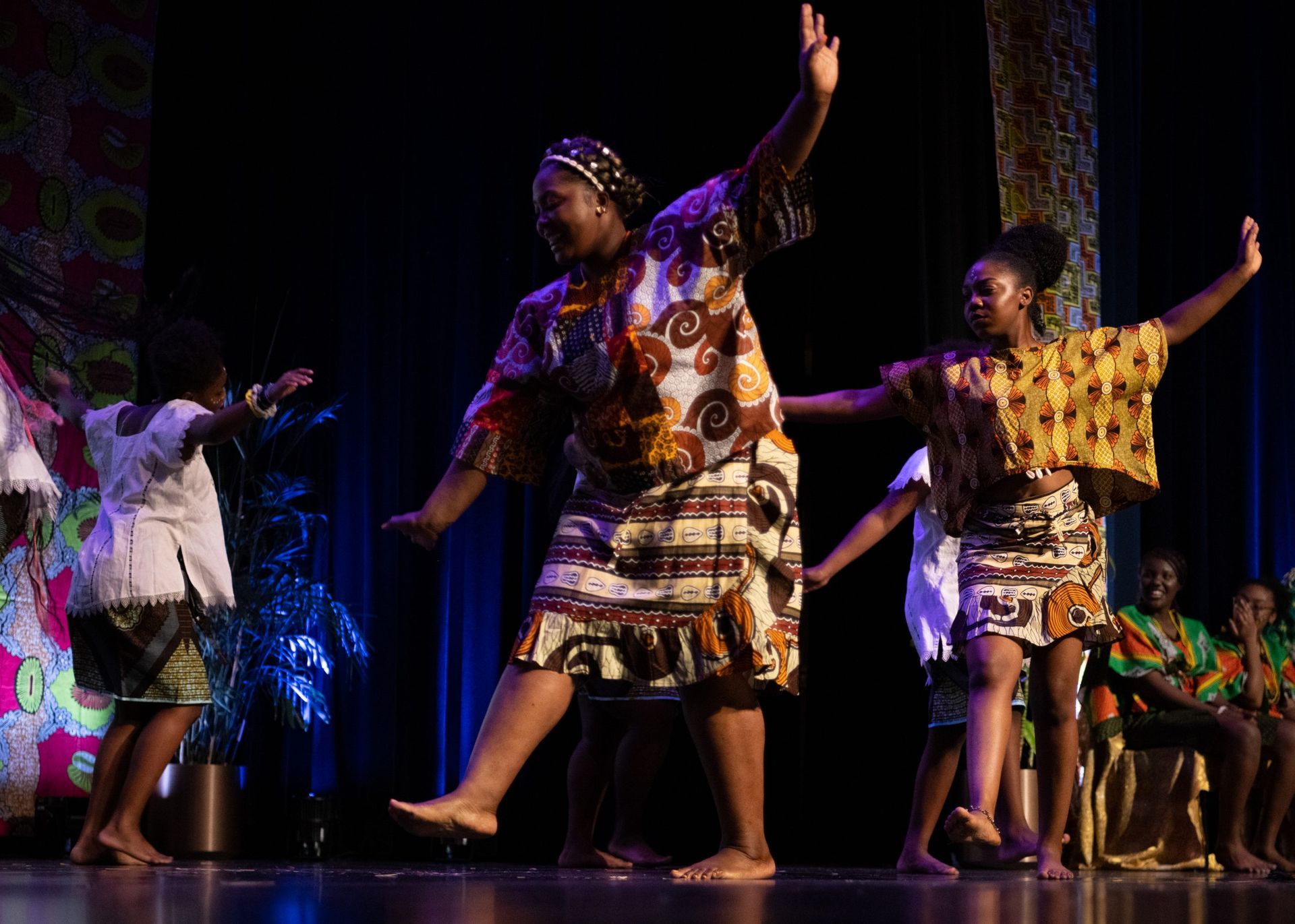 People in colorful African attire dance on a stage, lit by spotlights.