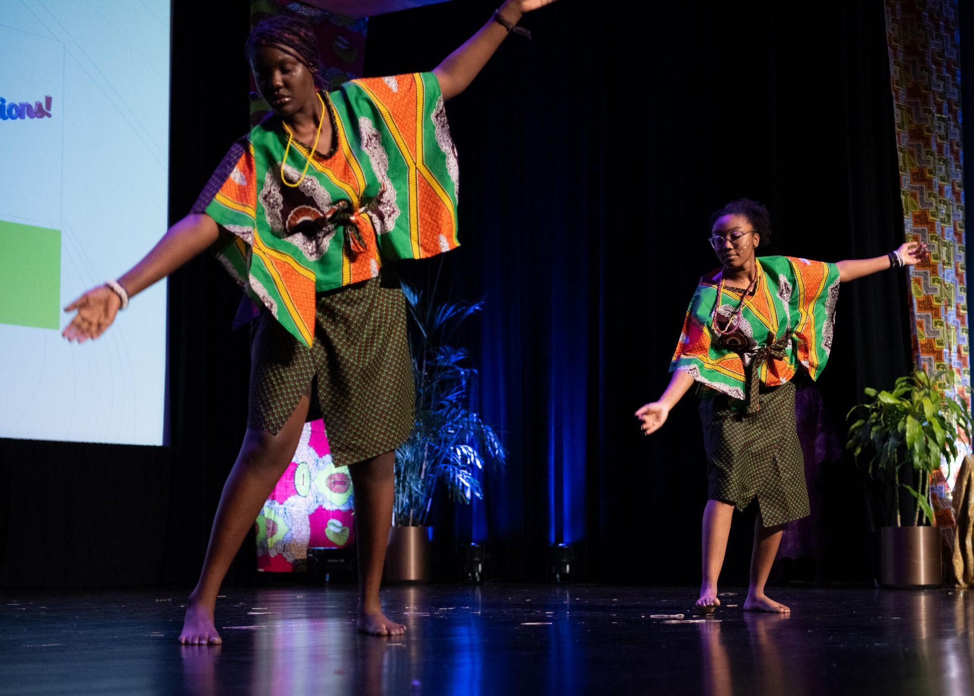 Two women in colorful African attire dancing on stage.