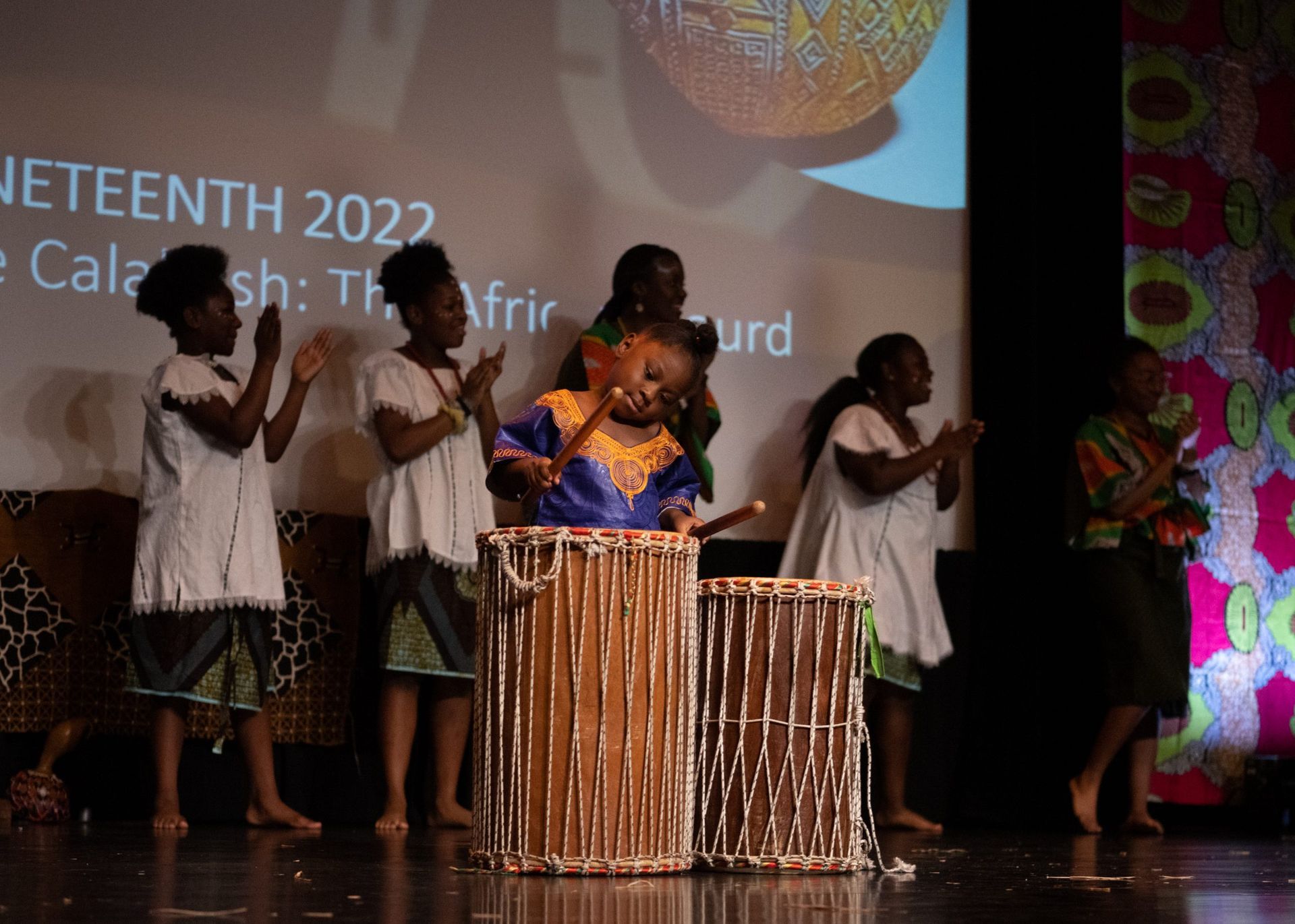 Children performing onstage: drummer, singers, Juneteenth 2022 event. Stage, cultural attire.