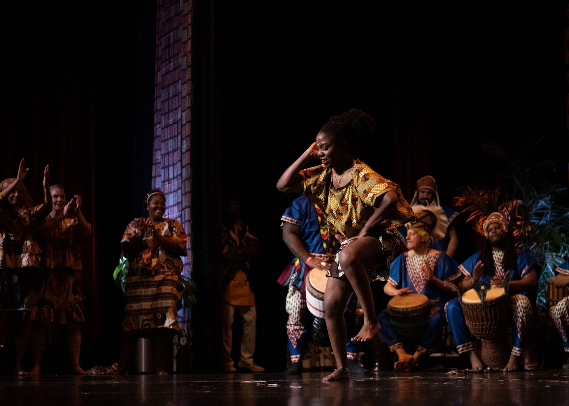 African dancer performing on stage with drummers and audience members.