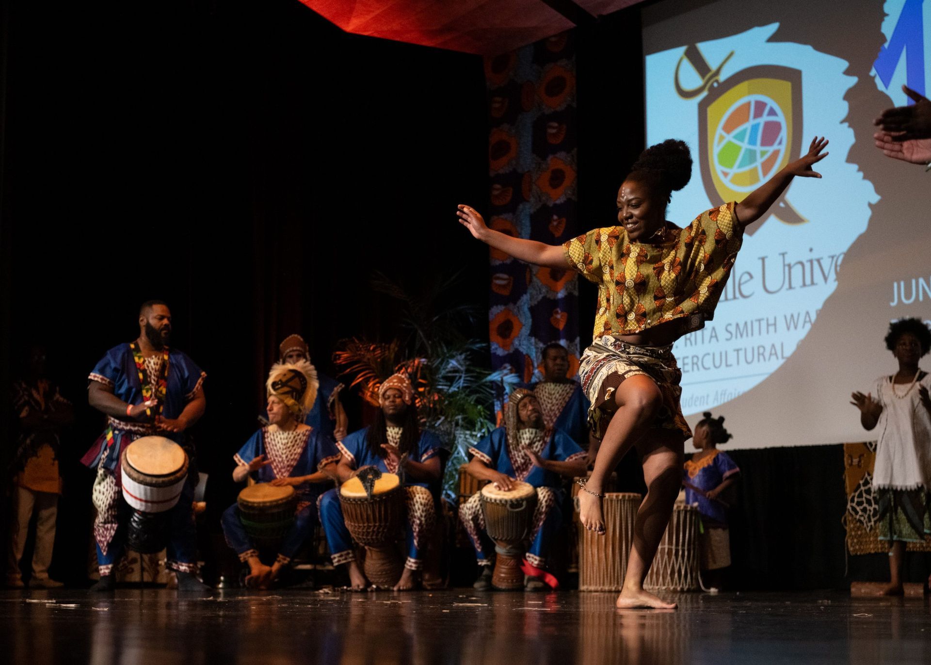 African dancer on stage with drummers in front of an audience.