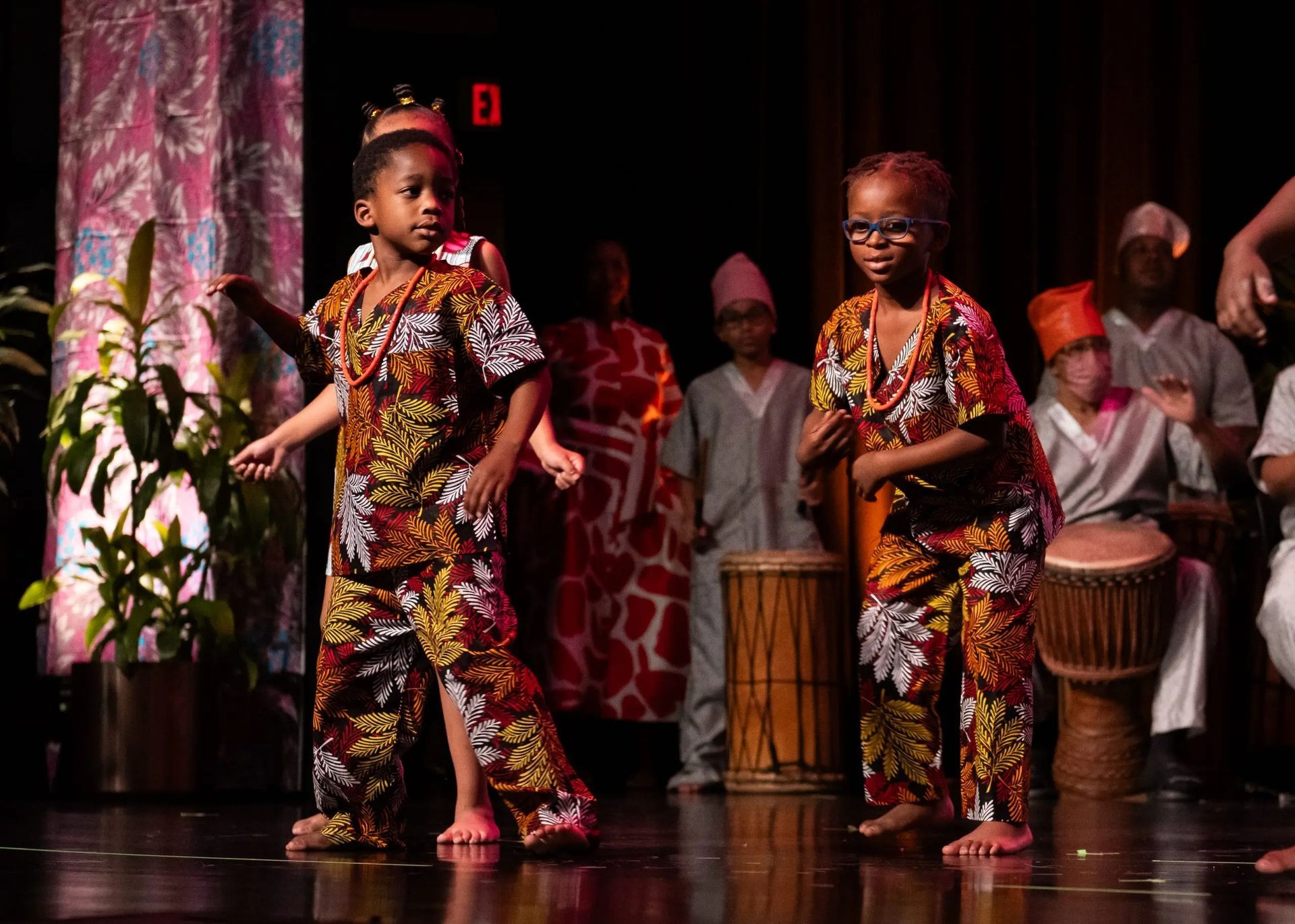Children in African attire dance on stage, drums in the background.