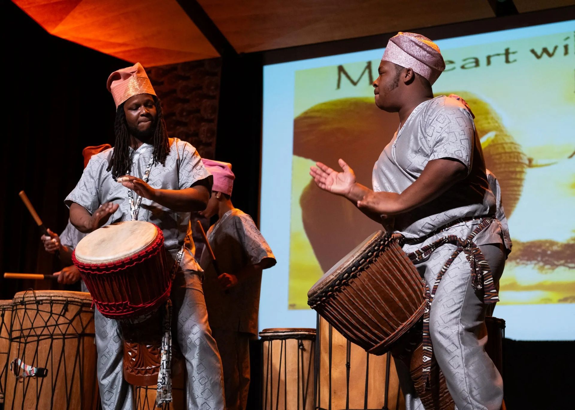 Men in African attire playing drums on stage.