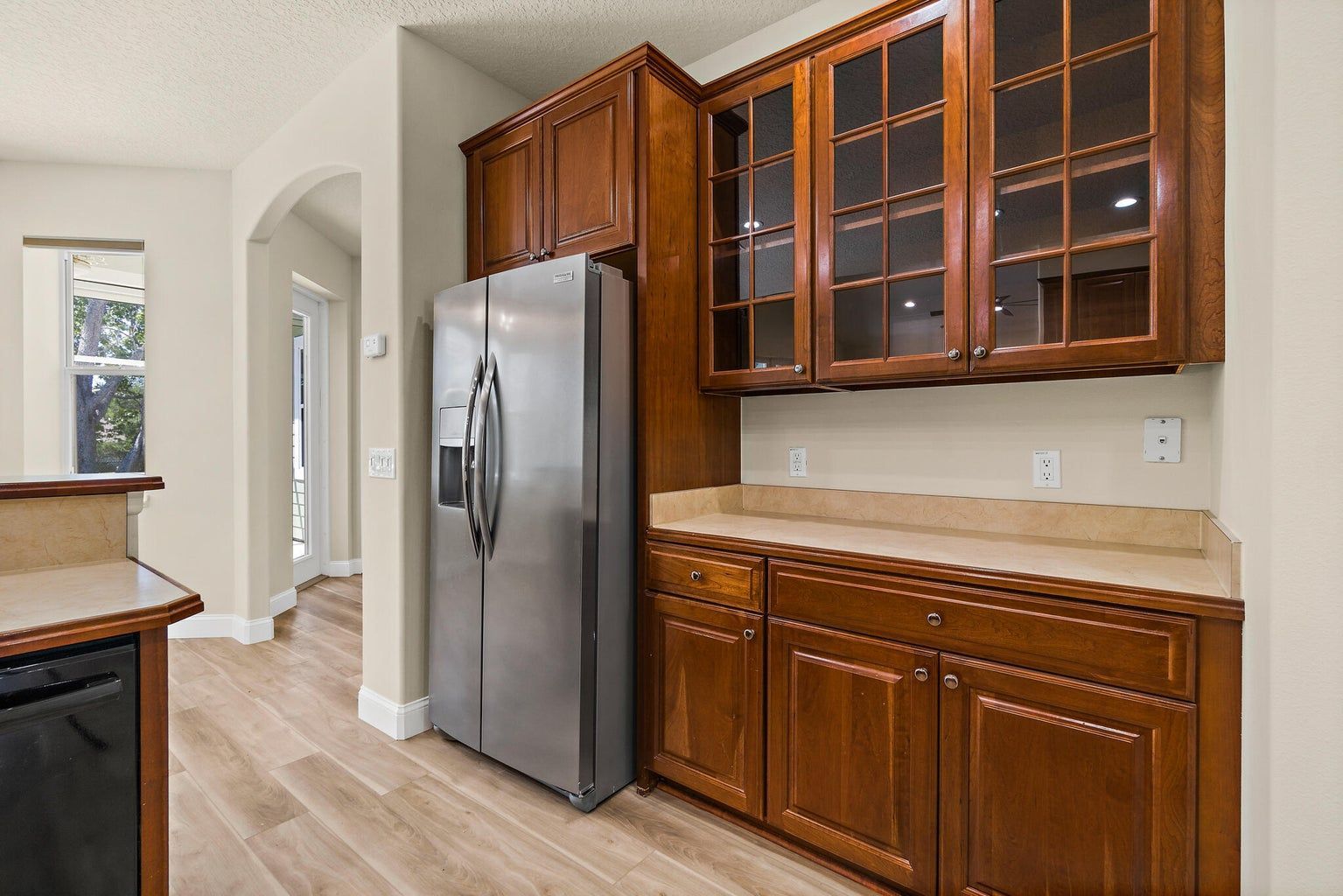 Green house with white trim, dormers, and front porch, set on a grassy lawn with trees, on a sunny day.