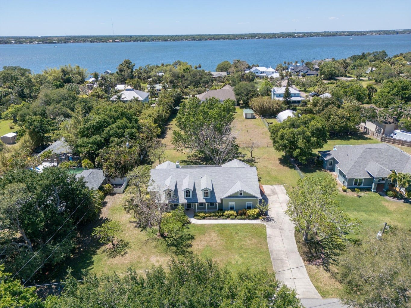 House with gray roof and blue-green siding overlooking a body of water, sunny day.