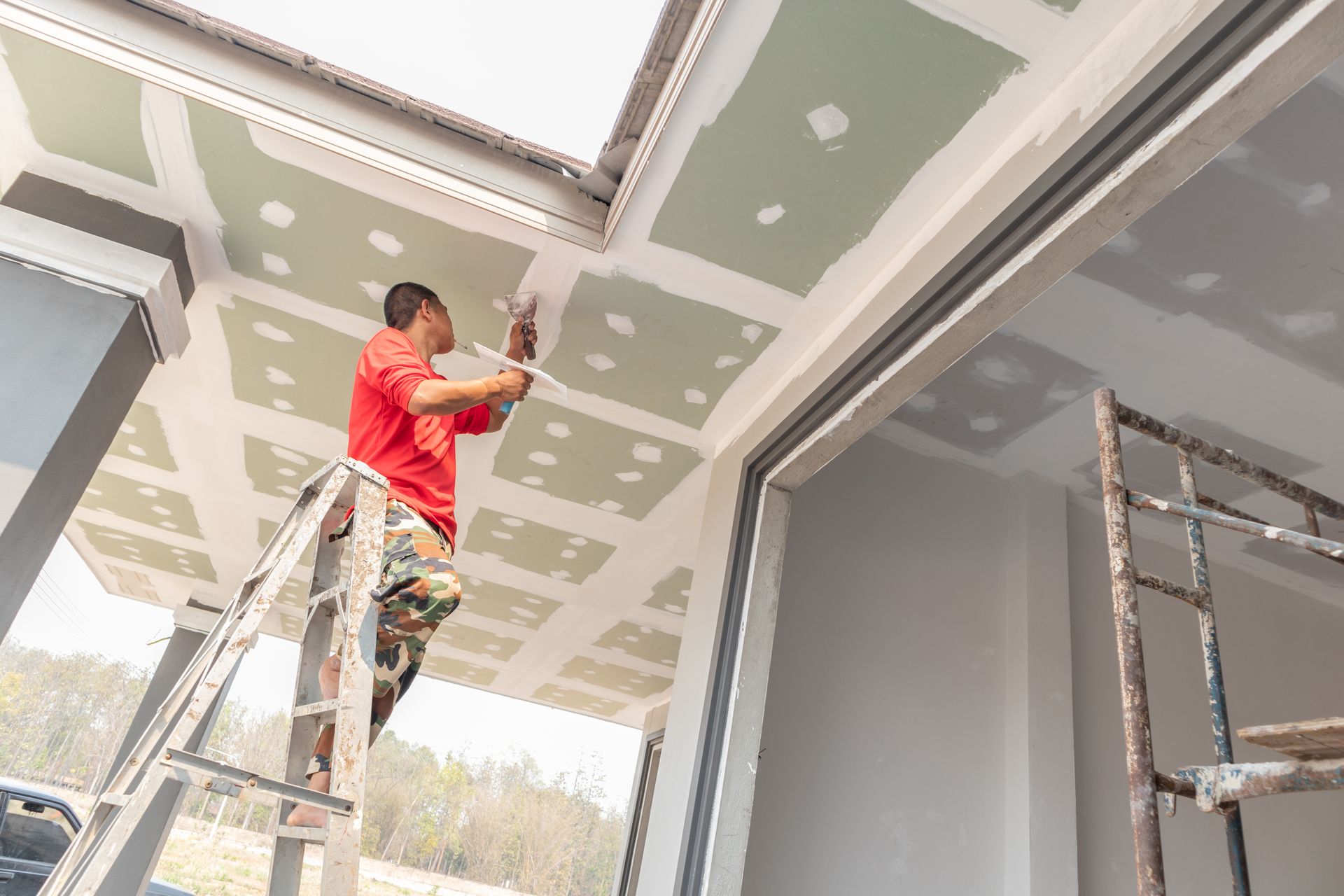 A man is standing on a ladder painting a ceiling.