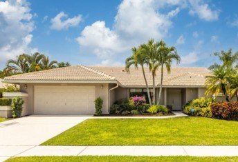A house with a lot of grass and palm trees in front of it.