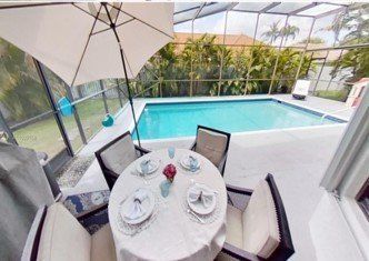 A table and chairs under an umbrella next to a swimming pool.