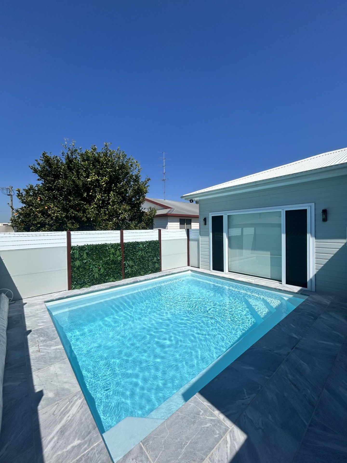 A small rectangular pool with clear water, a white building, and a green hedge against a blue sky — Clarence Valley Pools In Grafton, NSW