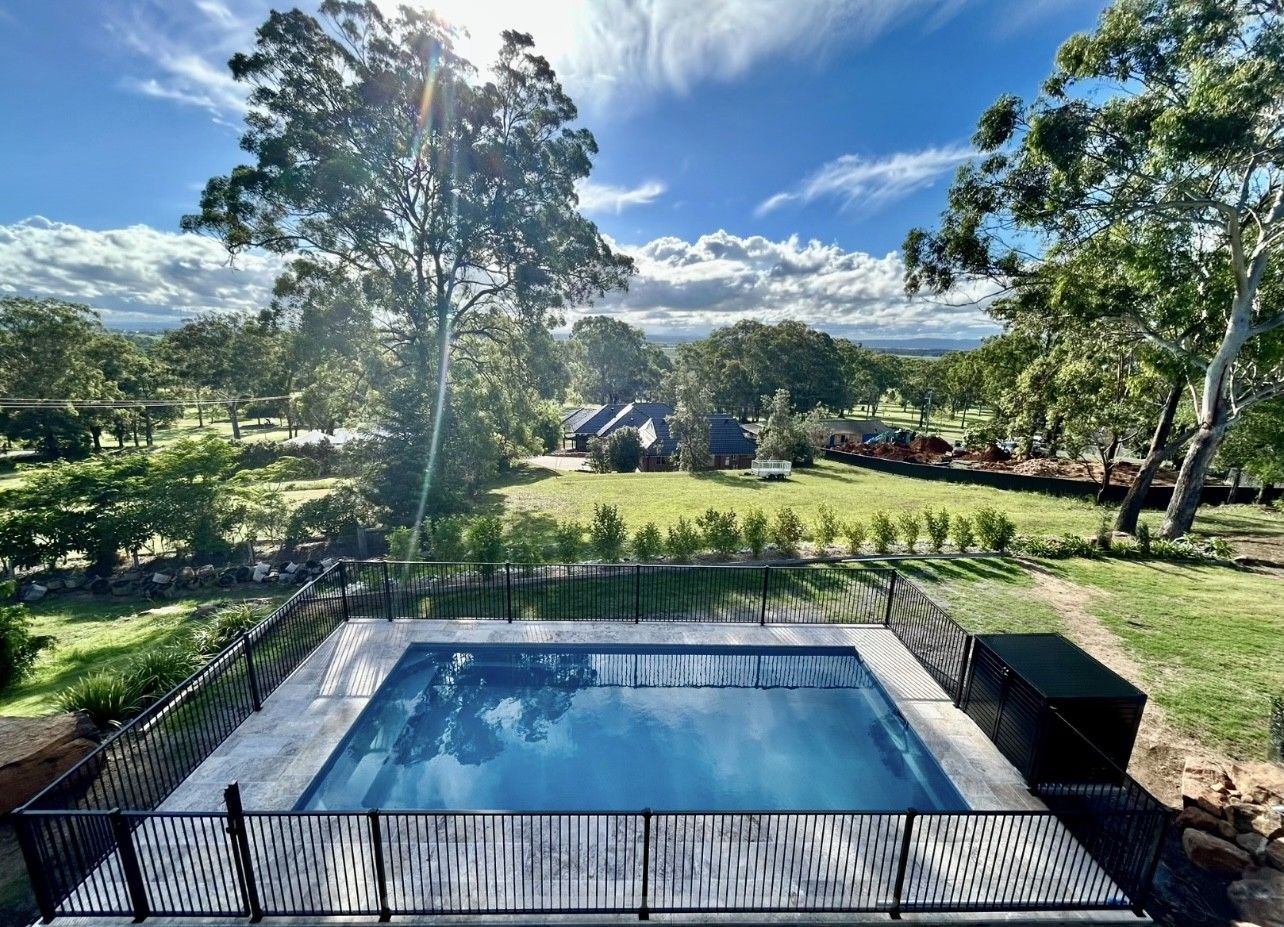Swimming pool surrounded by a fence, set in a green landscape with trees and a cloudy blue sky — Clarence Valley Pools In Yamba, NSW