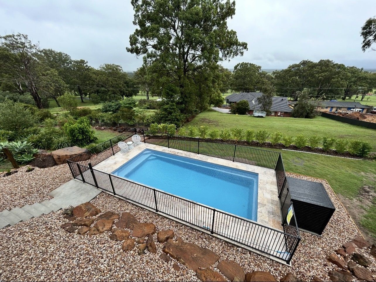 A rectangular swimming pool surrounded by a black fence, with a lush green landscape in the background — Clarence Valley Pools In Yamba, NSW