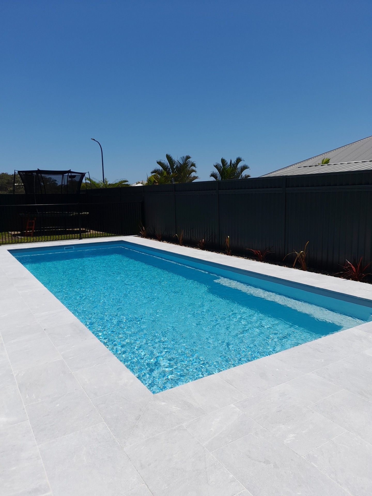Rectangular pool with bright blue water and light gray decking against a dark fence under a blue sky — Clarence Valley Pools In Yamba, NSW