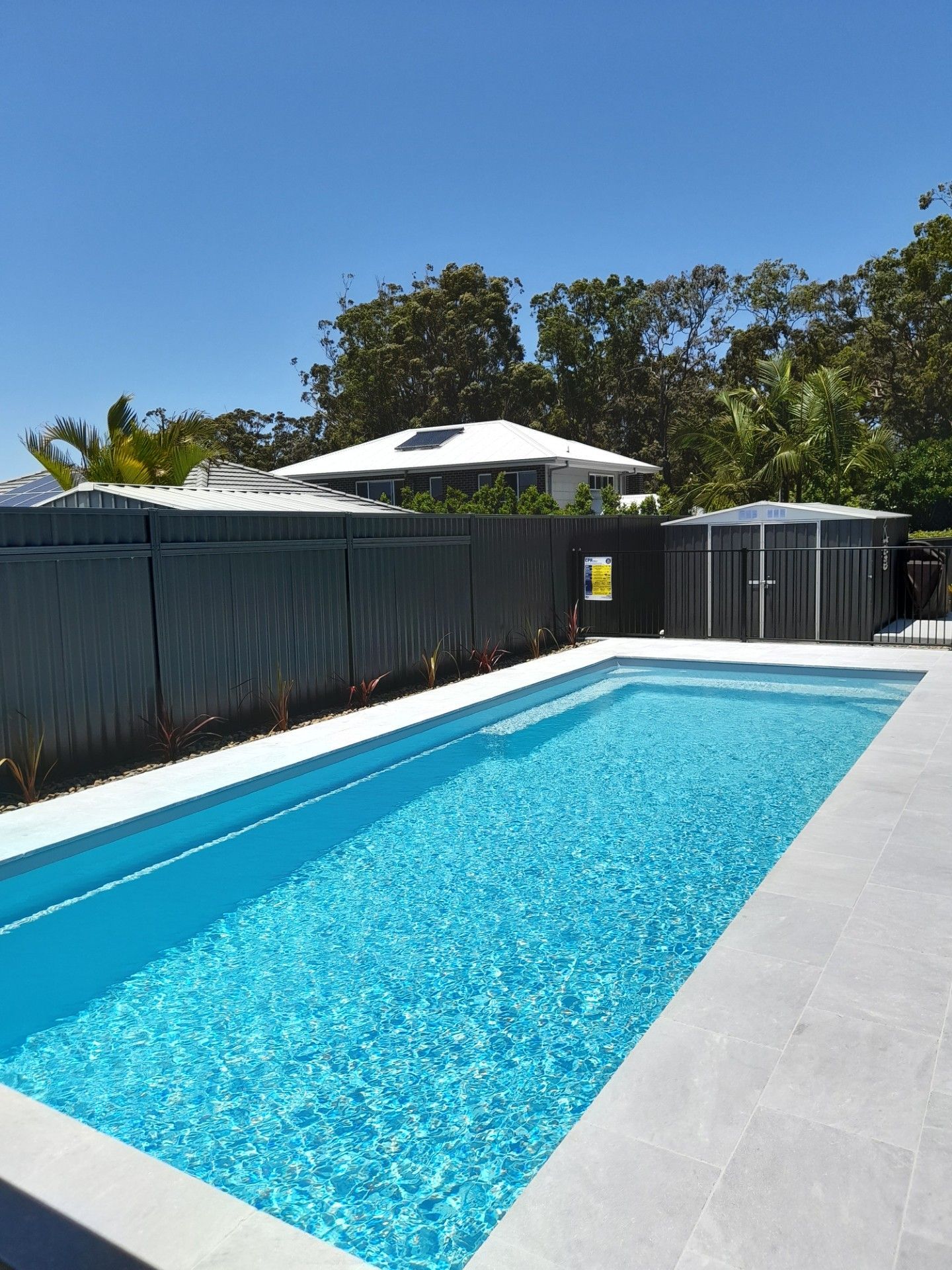 A rectangular pool with turquoise water, surrounded by grey paving, a fence, and a sunny sky — Clarence Valley Pools In Yamba, NSW