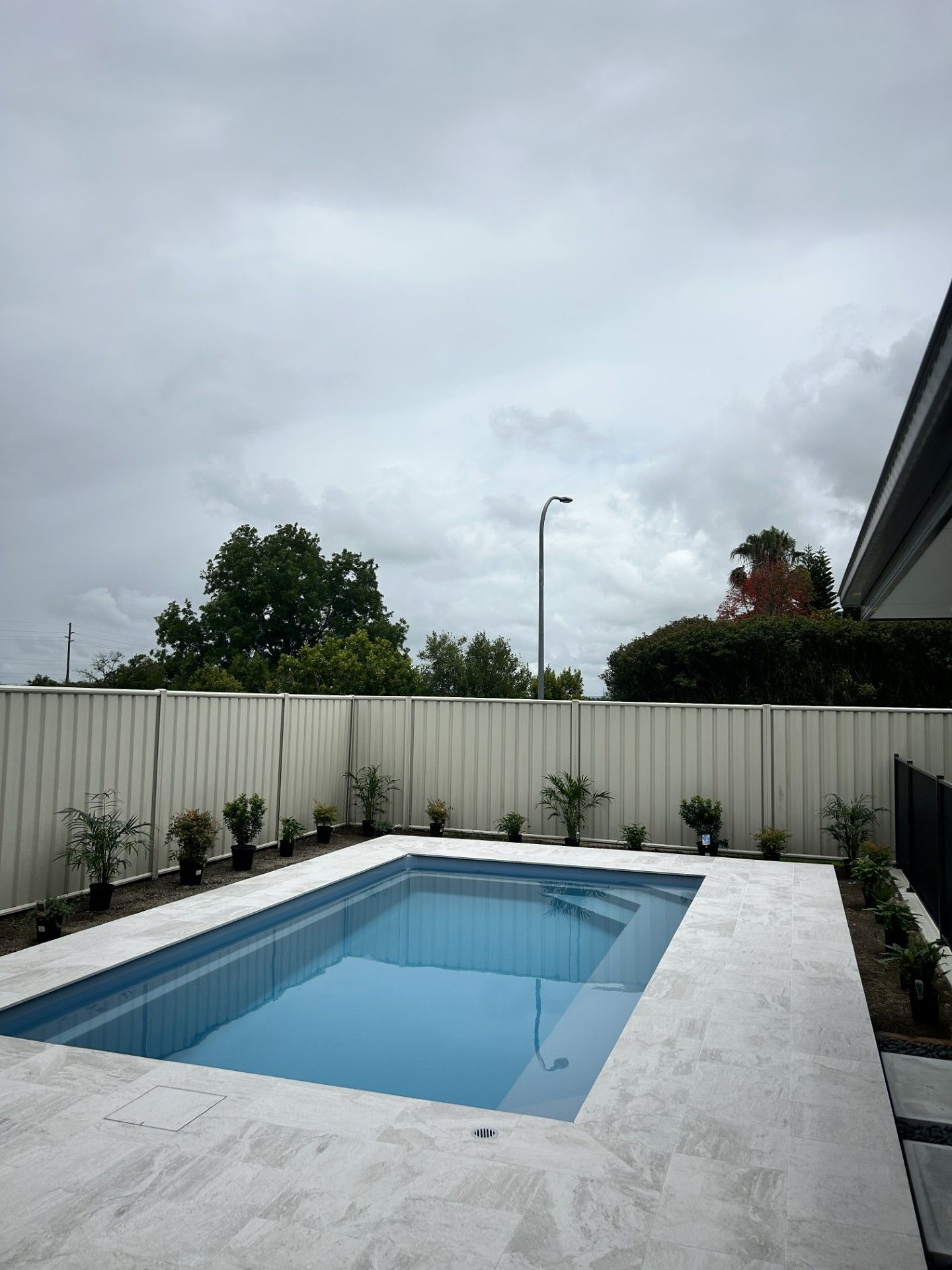 Rectangular swimming pool in backyard, bordered by concrete and a white fence under a cloudy sky — Clarence Valley Pools In Yamba, NSW