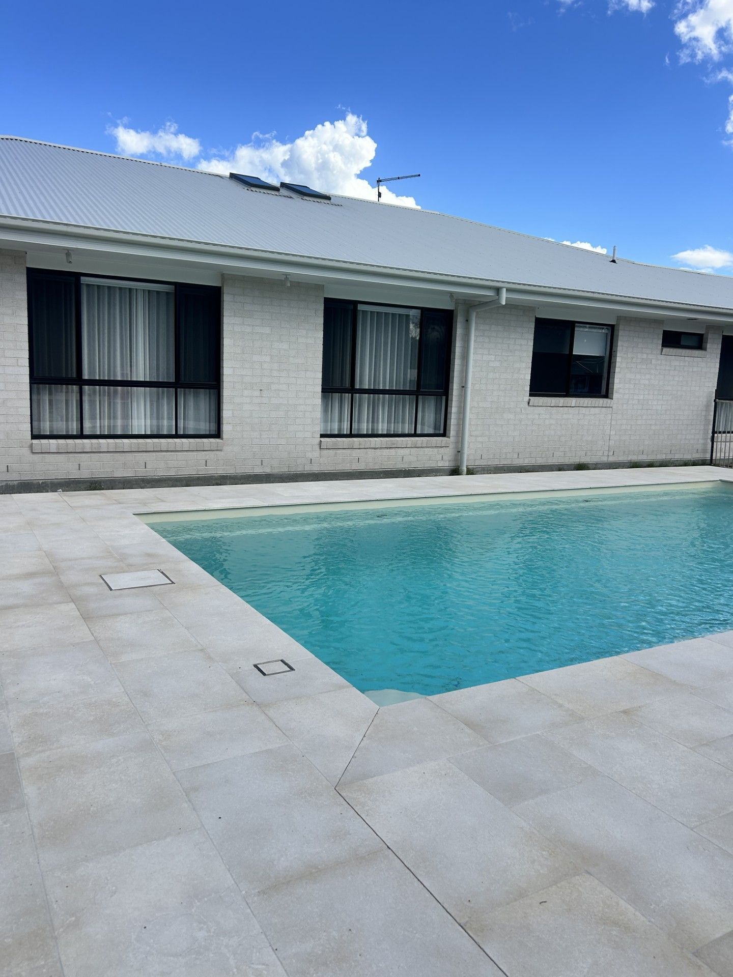 Pool with turquoise water in front of a white brick building with black window frames under a blue sky — Clarence Valley Pools In Yamba, NSW