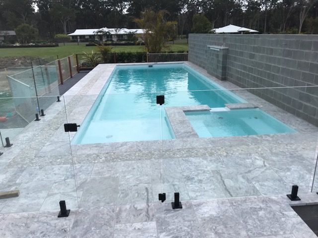 A Large Swimming Pool With a Glass Fence Around It — Clarence Valley Pools In Yamba, NSW