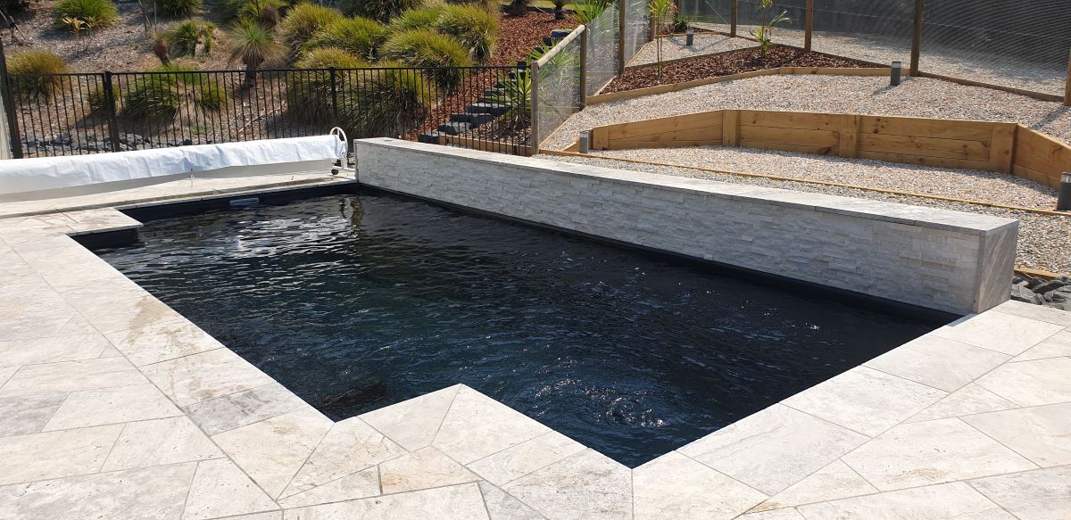 A Large Black Swimming Pool is Sitting on Top of a Tiled Patio — Clarence Valley Pools In Woolgoolga, NSW