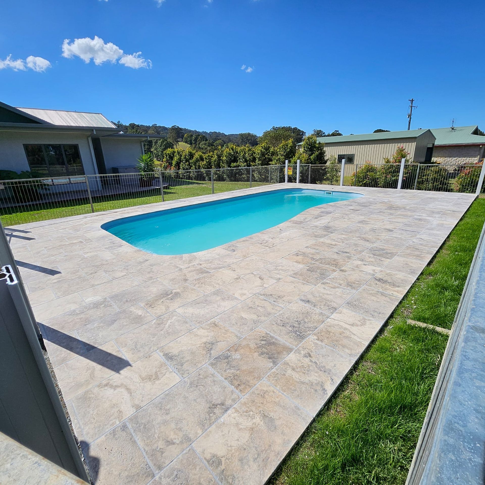 Pool with blue water surrounded by stone tiles and green grass, on a sunny day — Clarence Valley Pools In Yamba, NSW