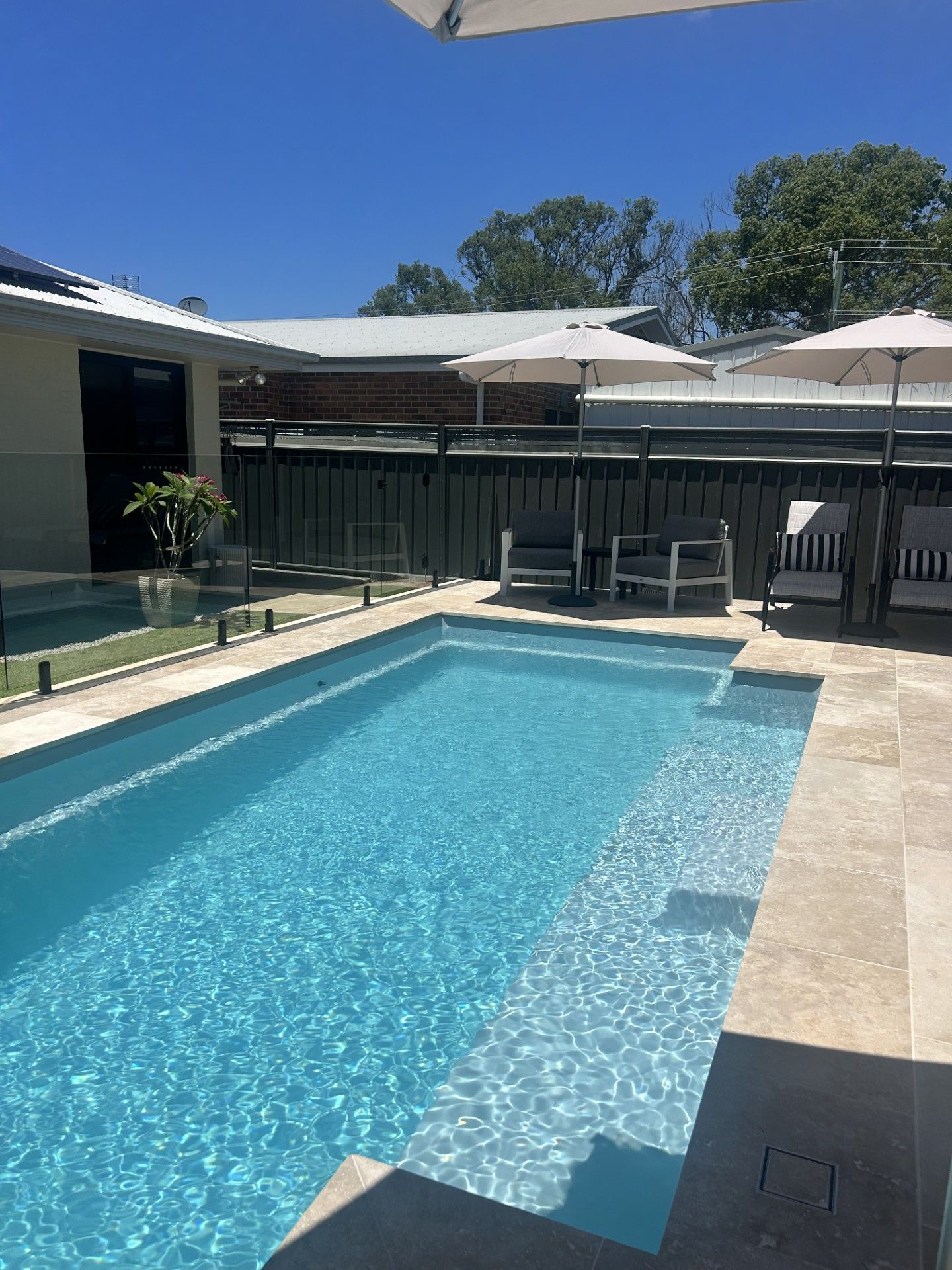Rectangular pool with turquoise water, patio furniture under umbrellas, and blue sky — Clarence Valley Pools In Yamba, NSW