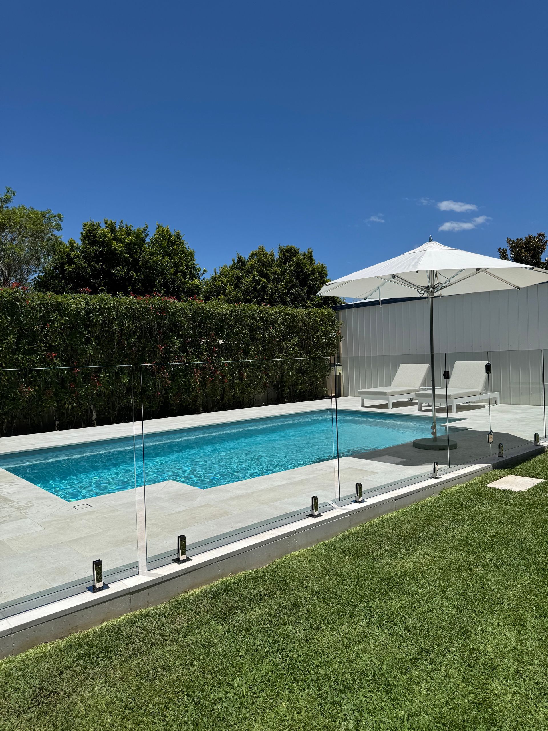 Swimming pool with turquoise water, white patio, and green lawn under a blue sky — Clarence Valley Pools In Yamba, NSW