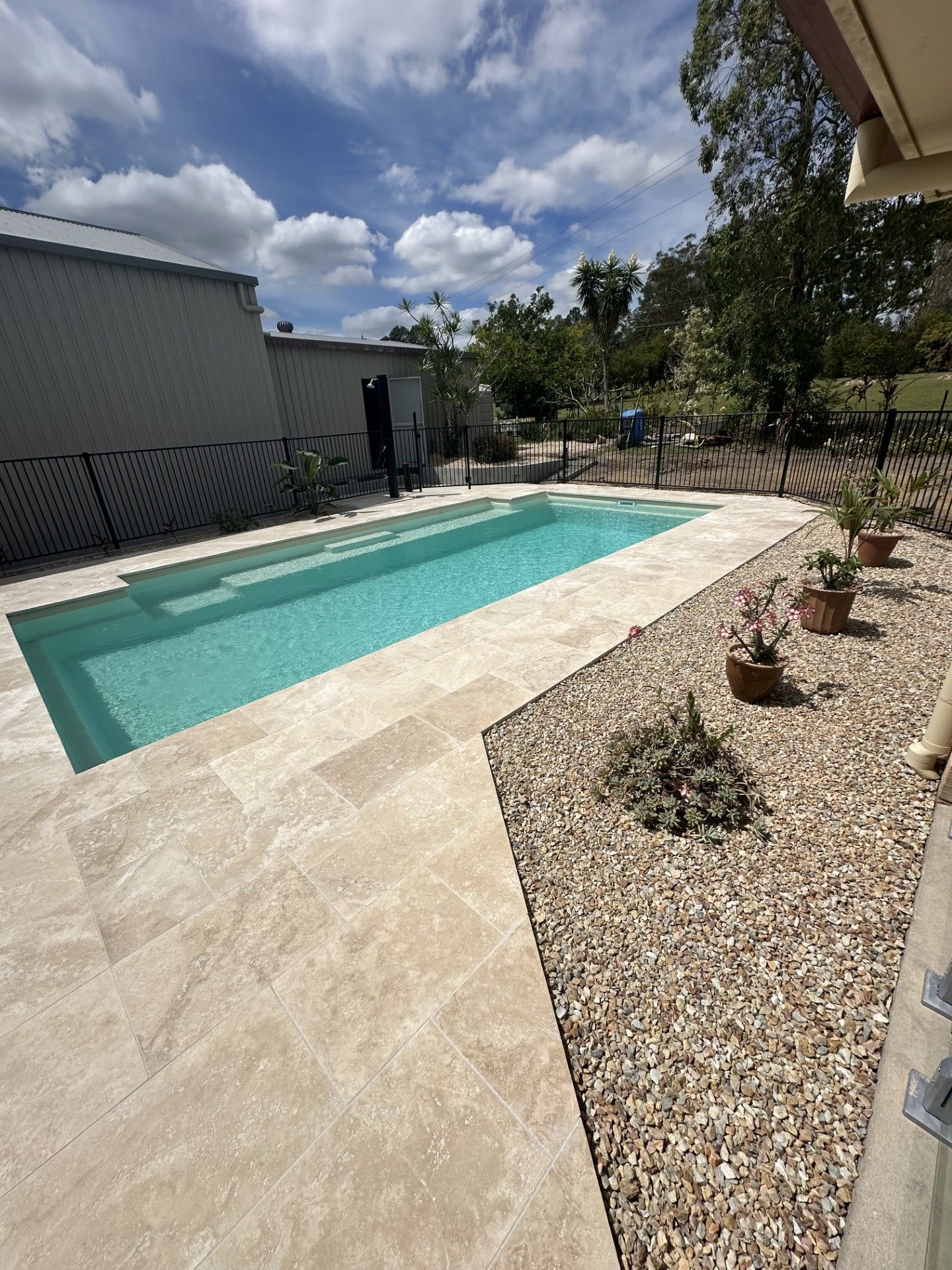 Rectangular turquoise pool with stone decking, gravel landscaping, and potted flowers. Grey shed in the background — Clarence Valley Pools In Yamba, NSW