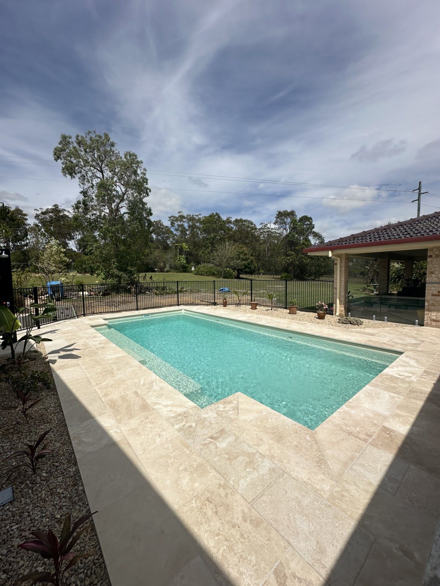 Rectangular pool with turquoise water, surrounded by light-colored paving. Sunny day with trees and a house in the background — Clarence Valley Pools In Yamba, NSW