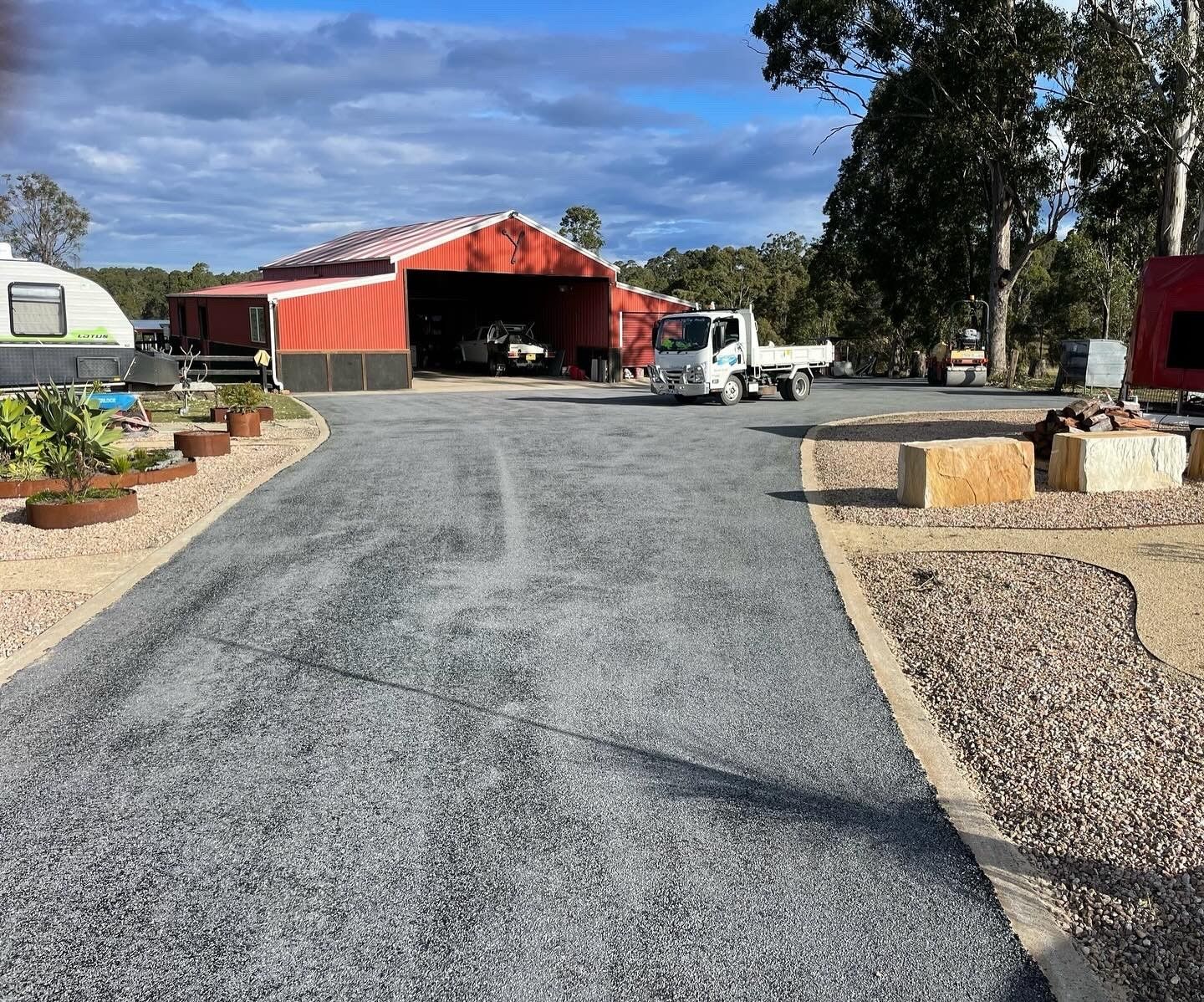 Gravel driveway leads to a red barn. A white truck is parked inside the barn. Landscaping with rocks — Clarence Valley Pools In Grafton, NSW