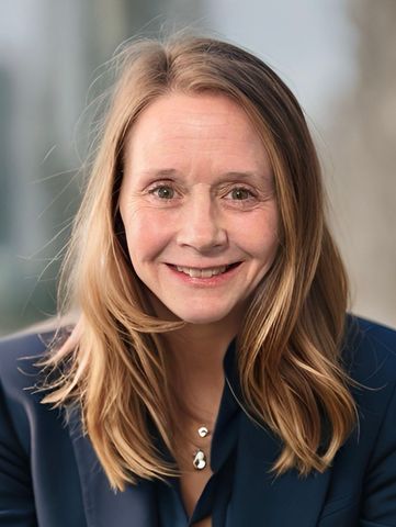 A woman wearing a blue jacket and a necklace is smiling for the camera.