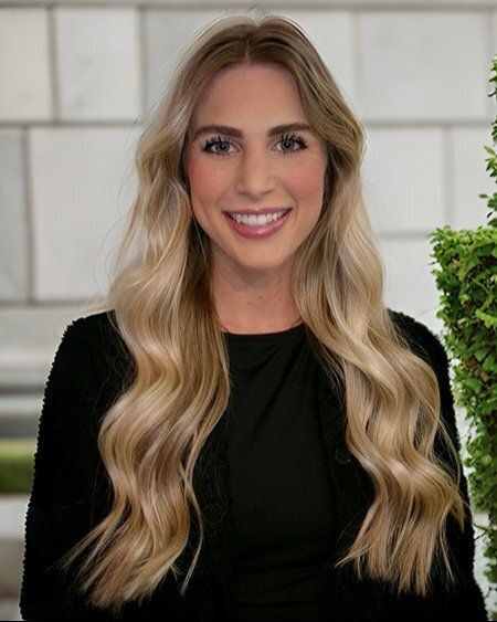 A woman with long blonde hair is wearing a black shirt and smiling.