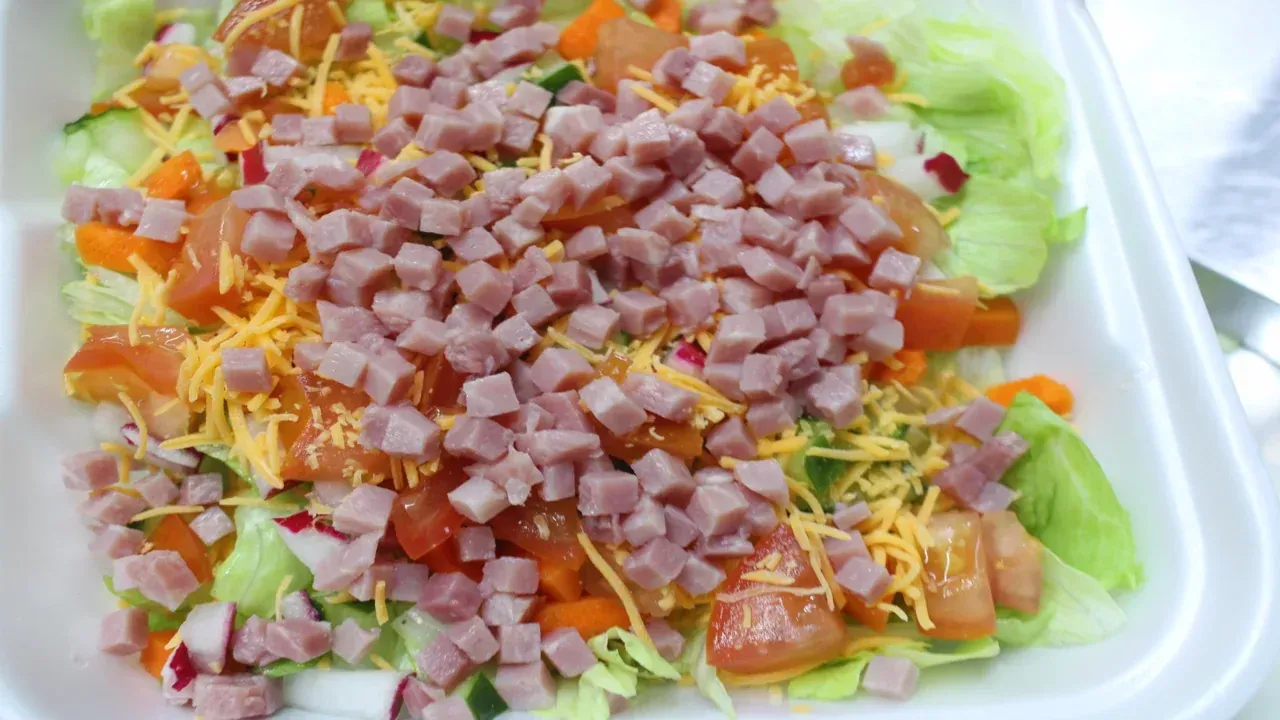 Chef salad: lettuce, chopped ham, shredded cheese, tomatoes, and carrots.