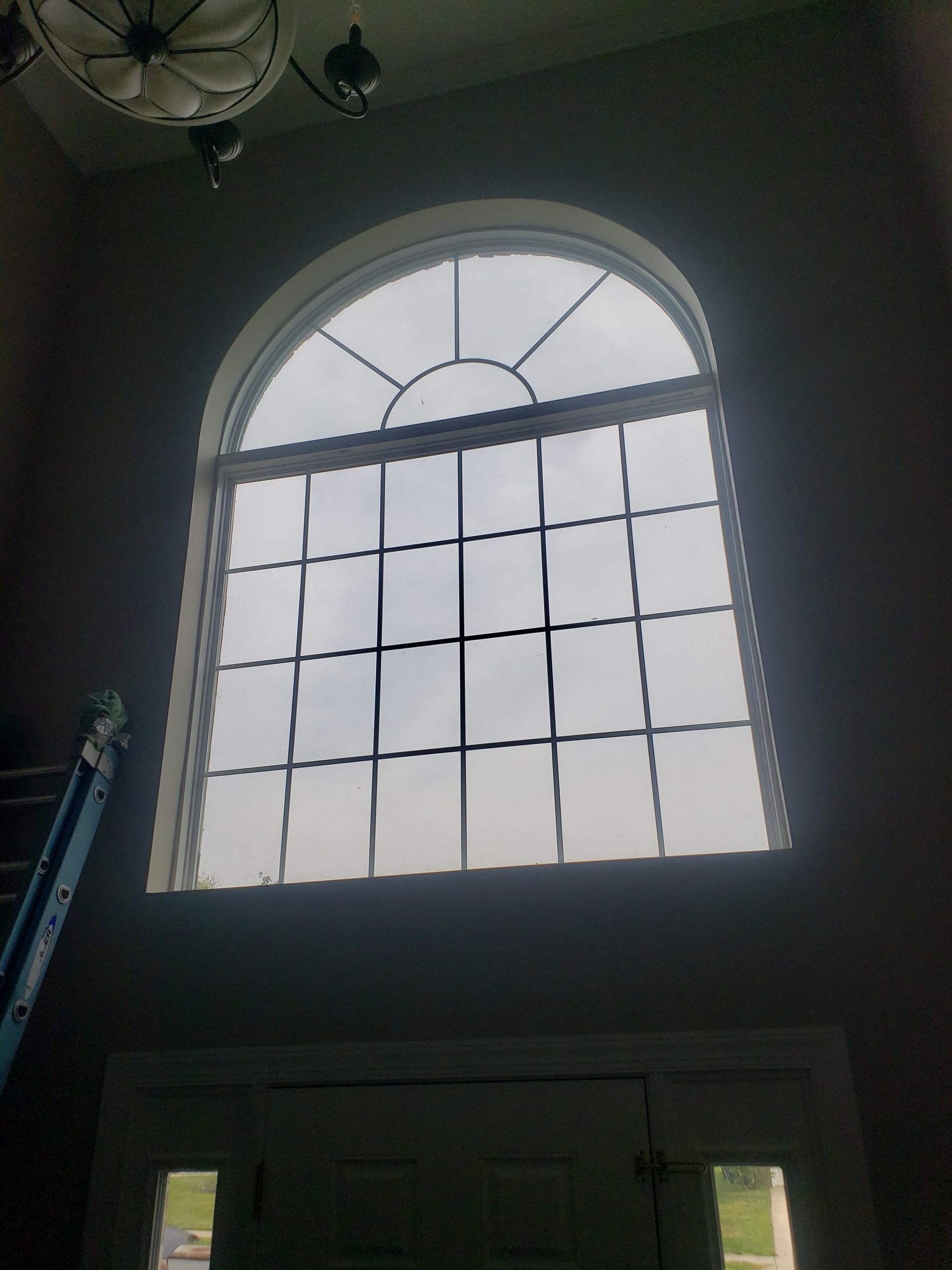 A large window in a dark room with a ladder in the background