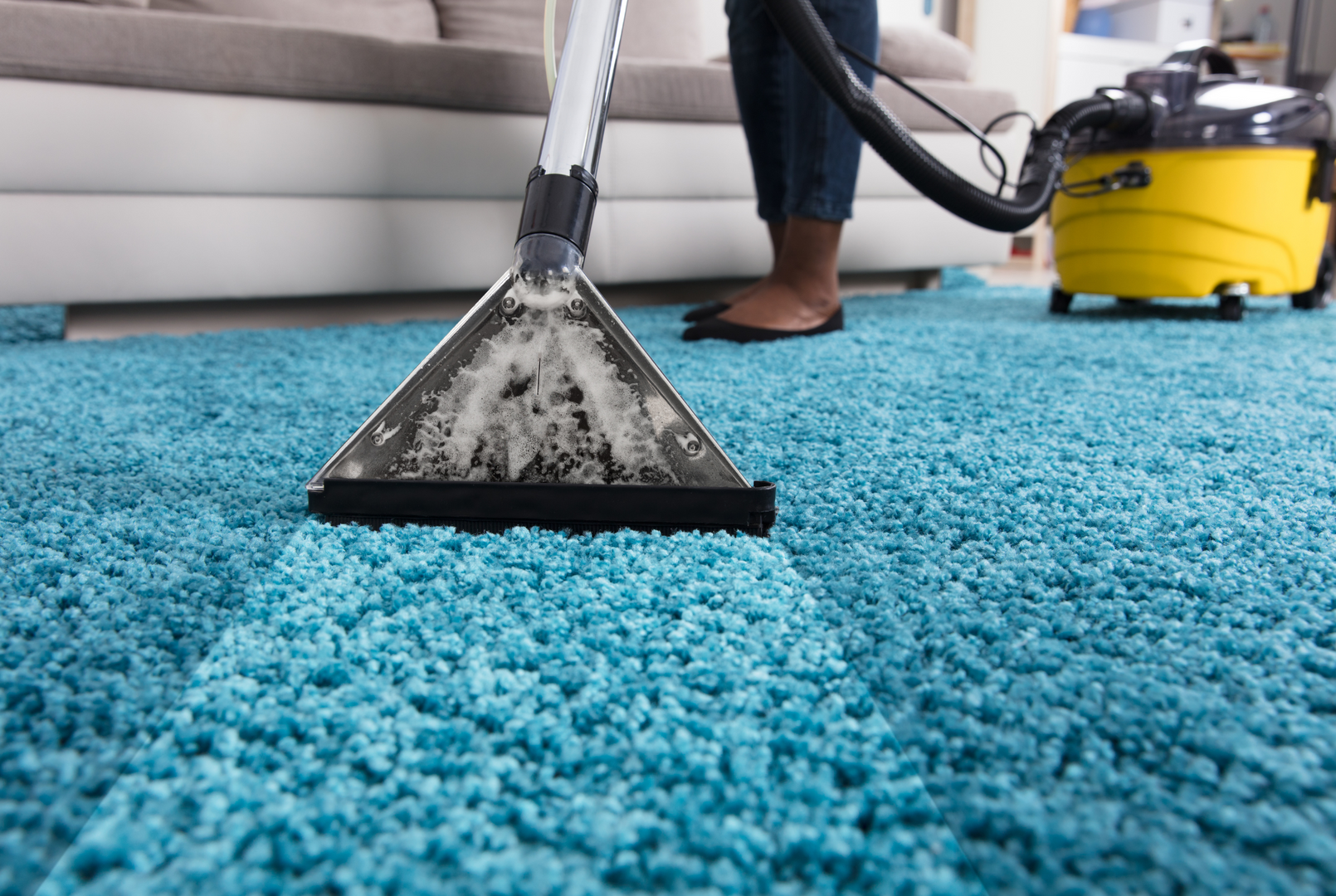 A woman is cleaning a blue carpet with a vacuum cleaner.