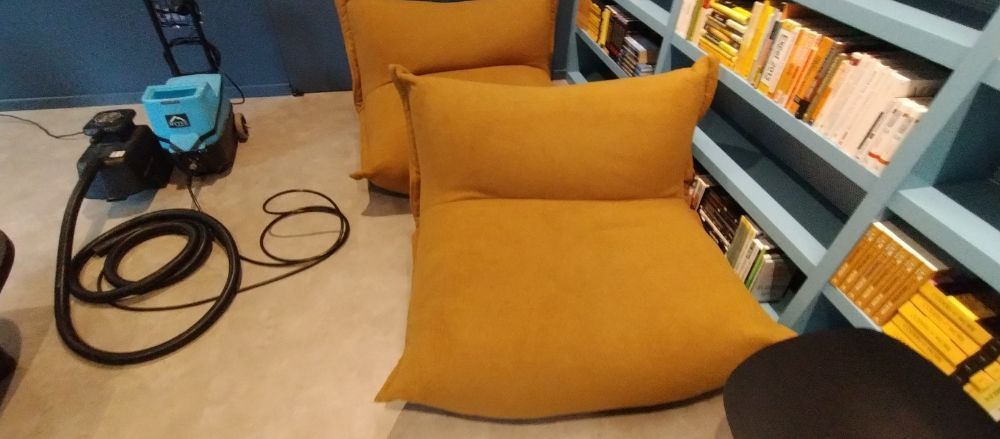 A vacuum cleaner is sitting next to a yellow bean bag chair in a library.