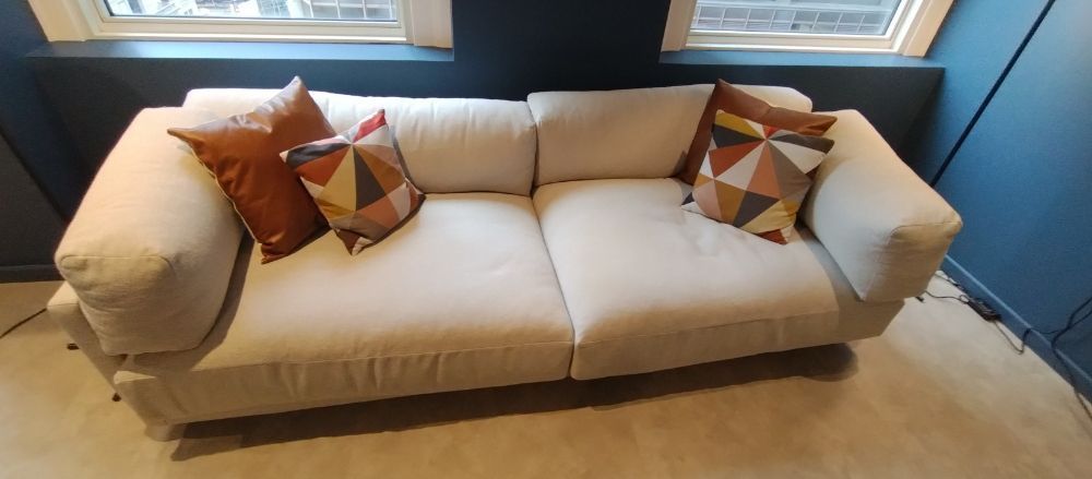 A white couch with colorful pillows is sitting in a room next to a window.