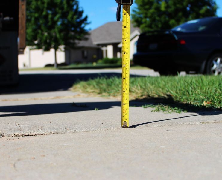 A yellow tape measure measures the height of a sidewalk