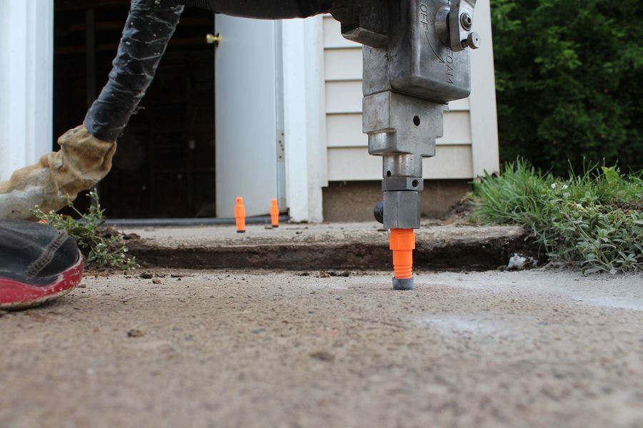 A person is using a drill on a sidewalk in front of a house.