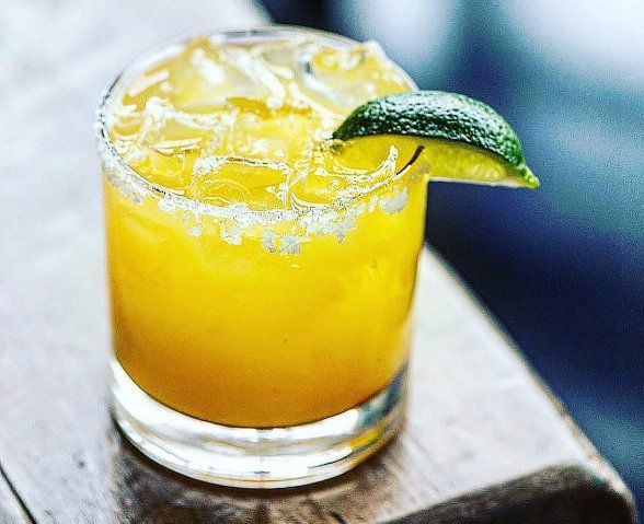 A close up of a margarita with a lime wedge on a wooden table.