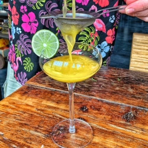 A person is pouring a yellow liquid into a martini glass