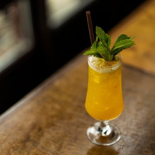 A glass of orange juice with a straw and mint leaves on a wooden table.