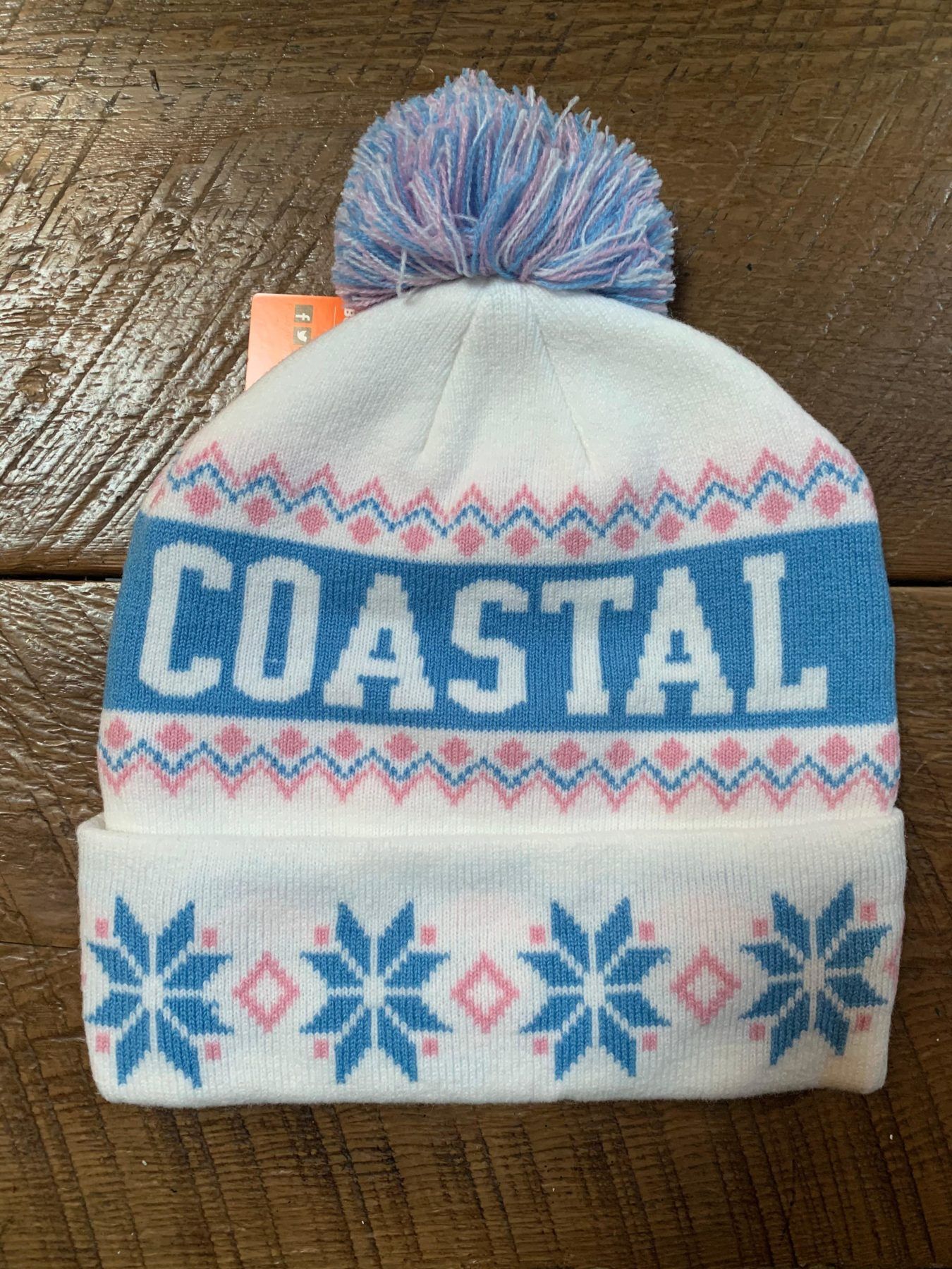 A white beanie with the word coastal on it is sitting on a wooden table.