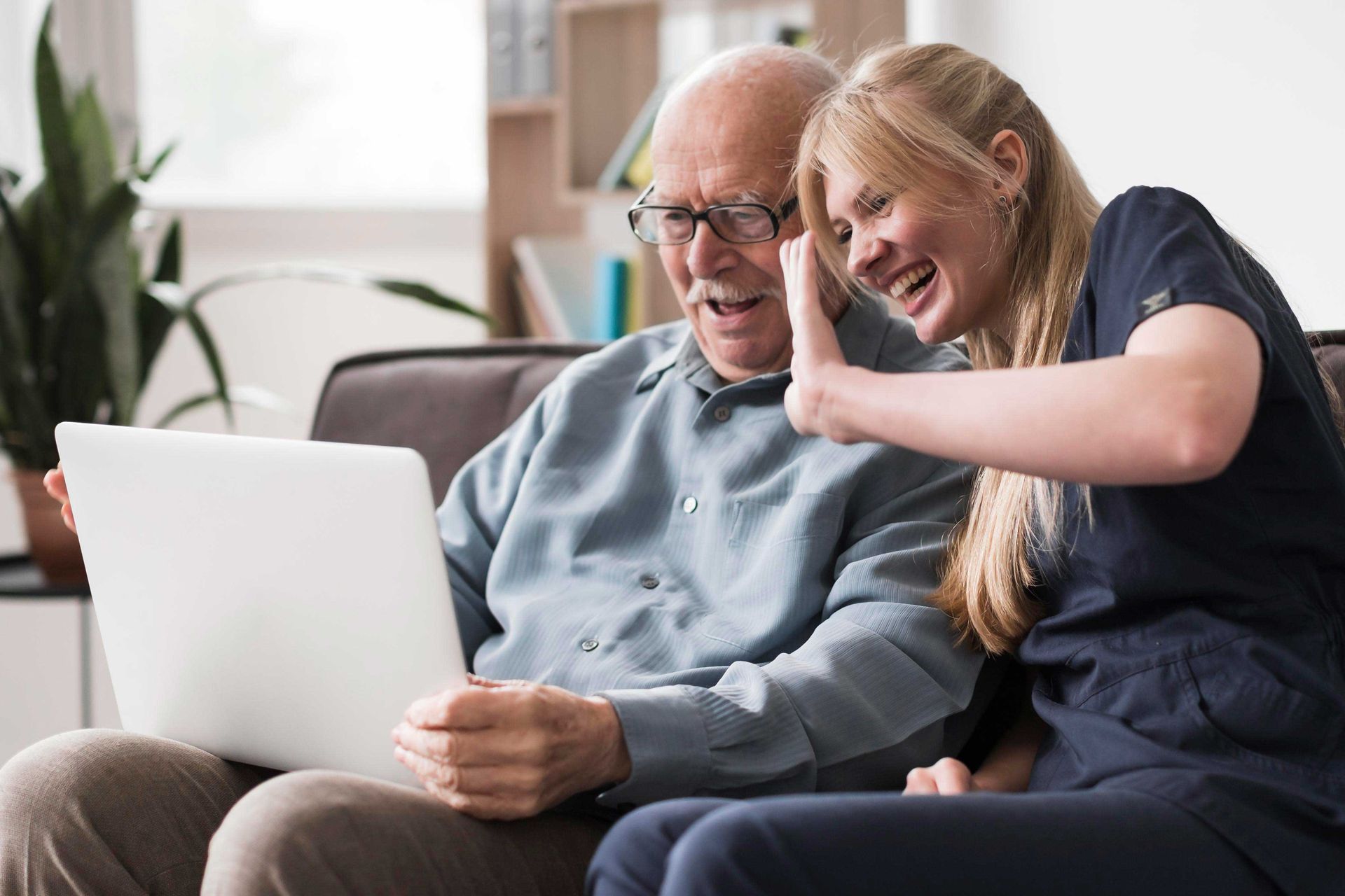 An elderly man and a young woman are sitting on a couch looking at a laptop.
