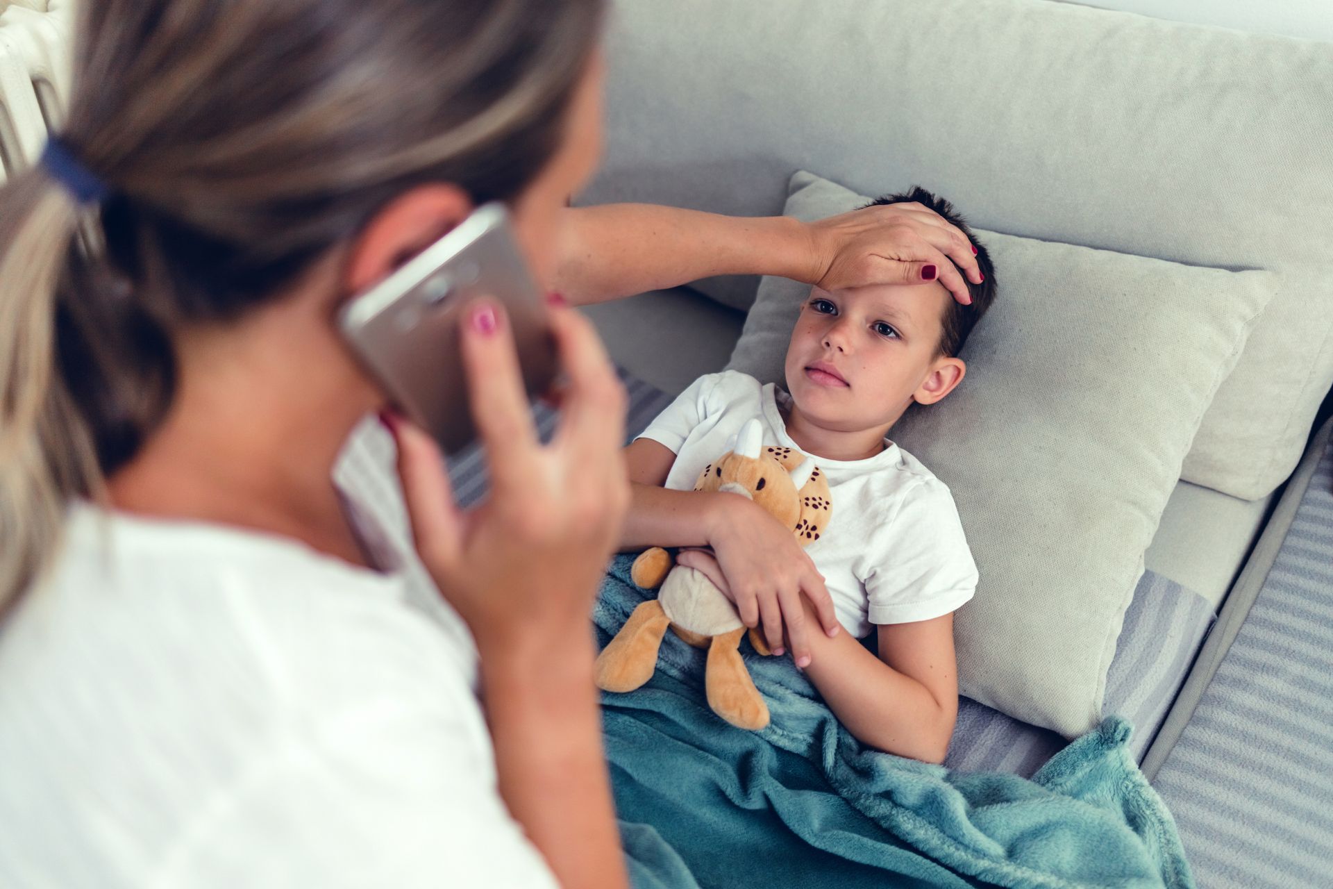 Boy with a fever holding a toy while mom is on phone making a call