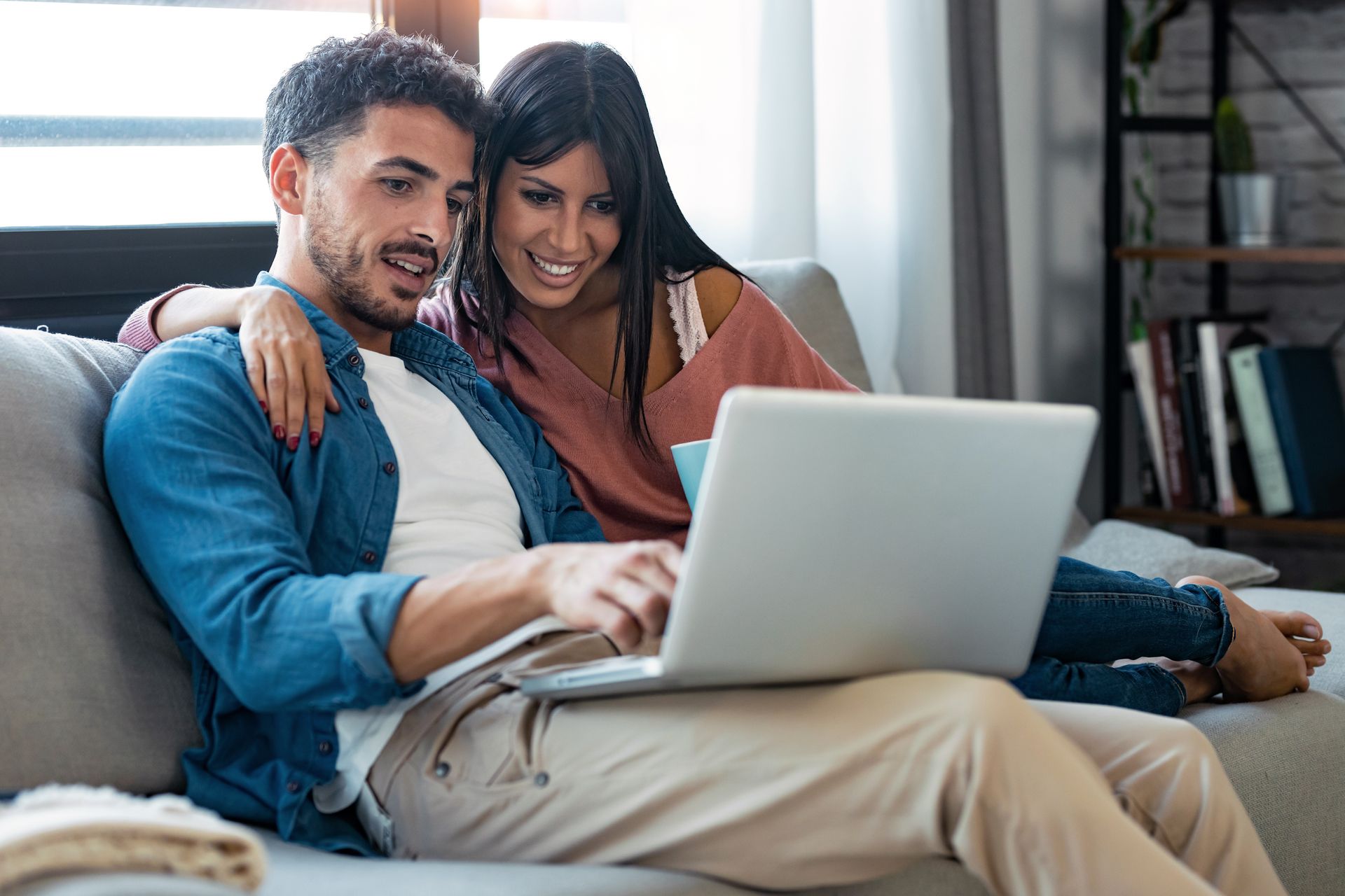 A man and a woman are sitting on a couch looking at a laptop.