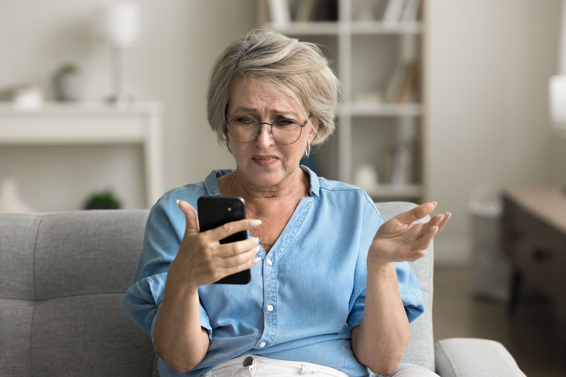 An older woman is sitting on a couch looking at her cell phone.