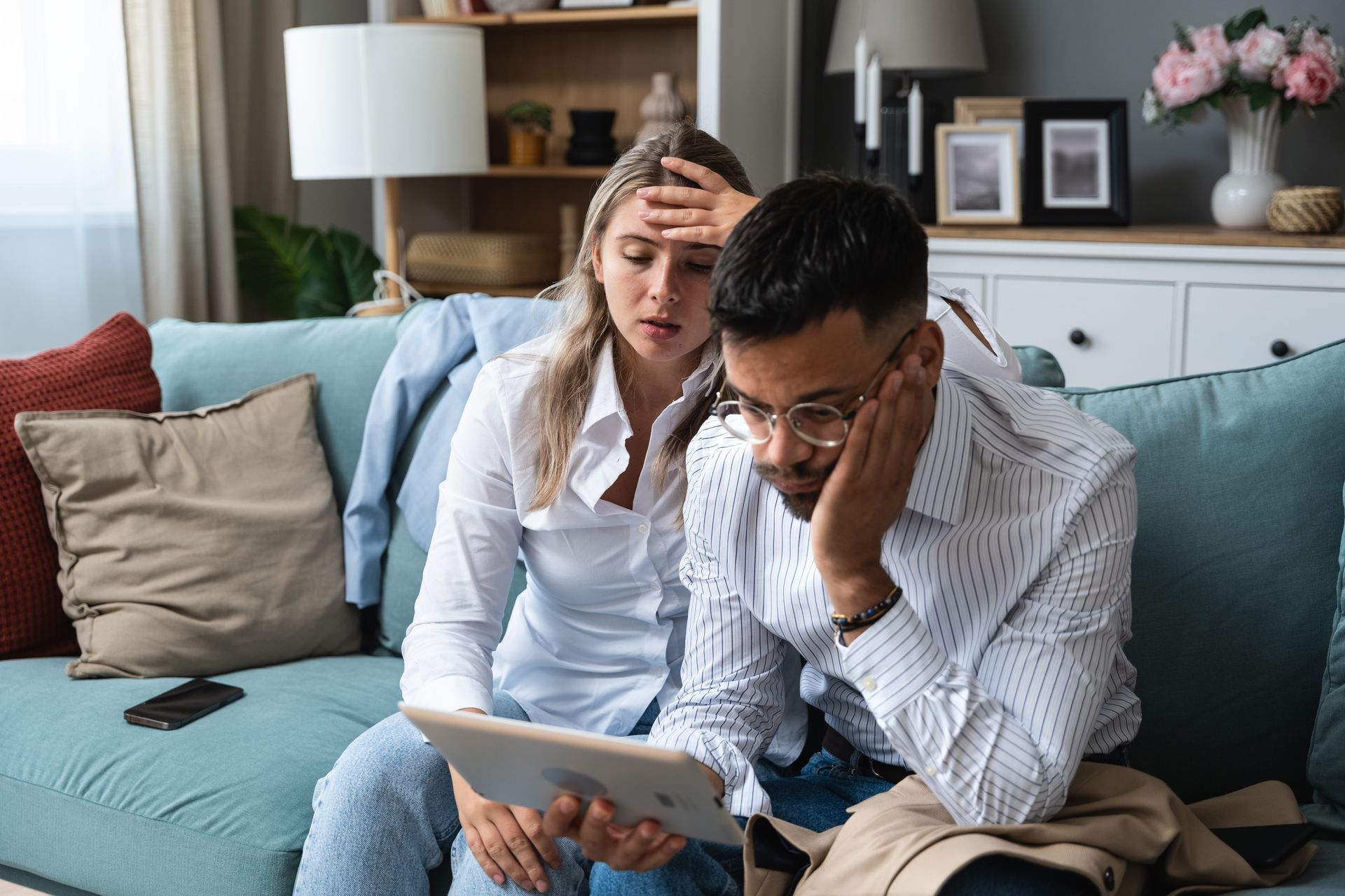 A man and a woman are sitting on a couch looking at a tablet.