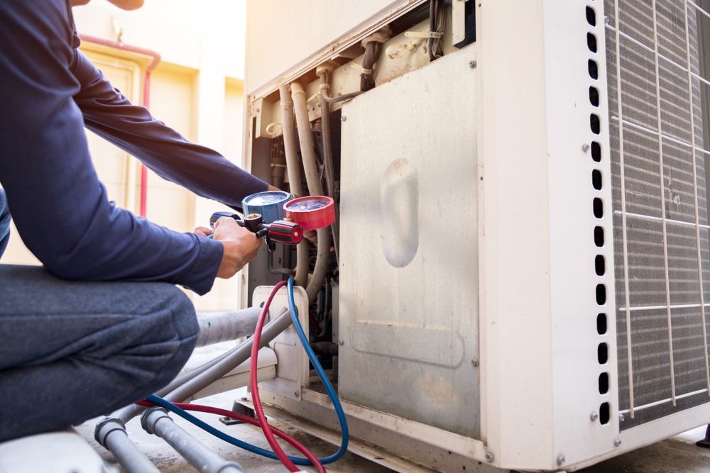A man is kneeling down to fix an air conditioner.
